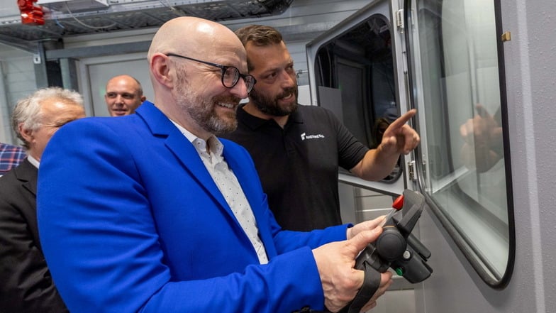 Einrichter Axel Czychon (großes Foto rechts) erklärt Wirtschaftsstaatssekretär Thomas Kralinski (links) bei Pierburg das Beschichten der Elemente von Kondensatoren mit einem Laser.r