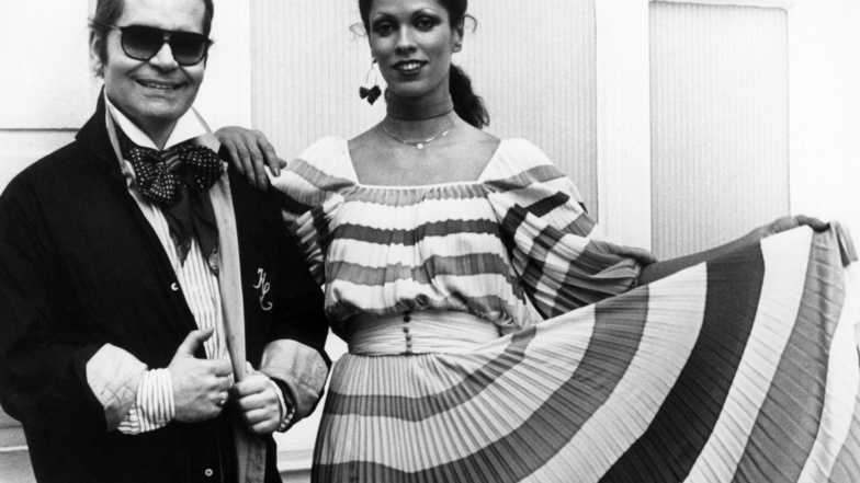 1977: Modeschöpfer Karl Lagerfeld neben einem Model in einem Plissee-Kleid aus Lagerfelds Chloe-Kollektion.