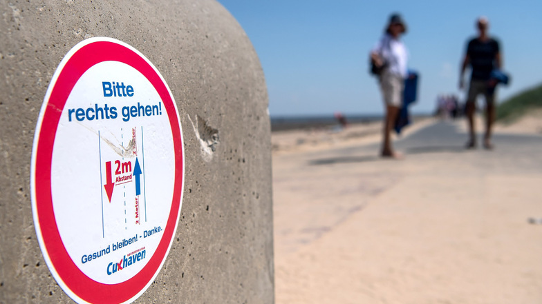 Niedersachsen, Cuxhaven: Ein Schild am Strand weist auf die vorgeschriebenen Laufrichtungen und Sicherheitsabstände hin. 