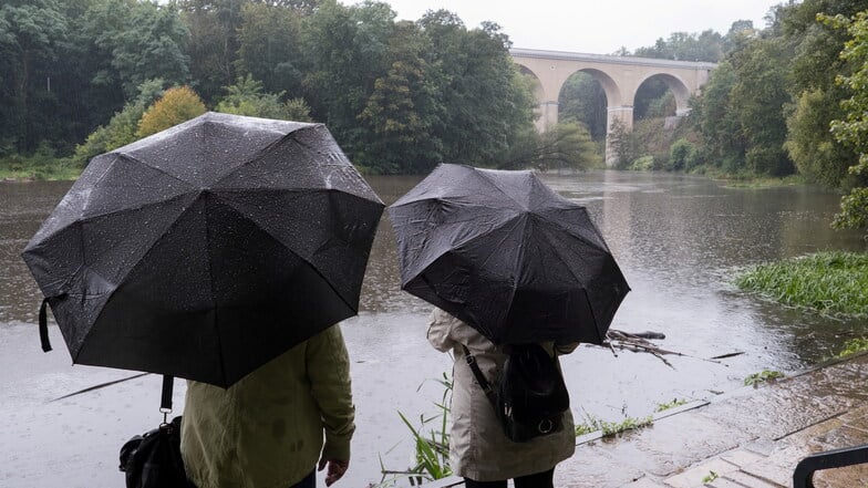 Passanten mit Regenschirmen schauen bei starkem Regen in Görlitz auf die Neiße beim Viadukt nahe der Obermühle.