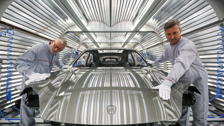 Zwei Porsche-Mitarbeiter prüfen in der Lackiererei den Lack der Karosserie eines vollelektrischen Porsche Macan im Werk Leipzig. Am selben Tag wurde der offizielle Start der Elektromobilität in Leipzig gefeiert.  Foto:dpa