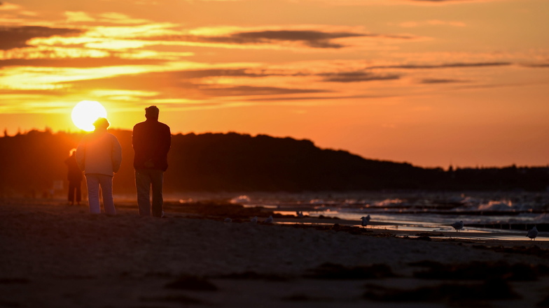 Spaziergänger sind bei Sonnenuntergang am Strand der Ostsee in Zempin auf Usedom unterwegs.