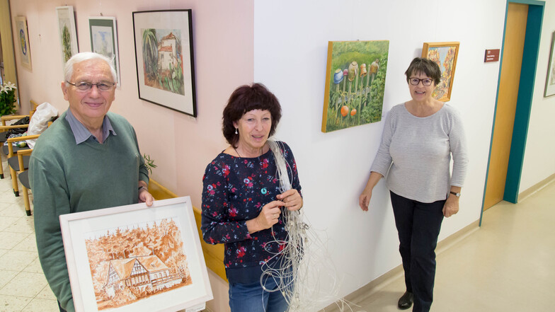 Horst Pinkau (links) und Anita Giesbers (rechts) von der Regionalgruppe Löbau des Oberlausitzer Kunstvereins hängen mit der Nieskyer Künstlerin Gabriele Beinlich im Krankenhaus Emmaus die Bilder auf.