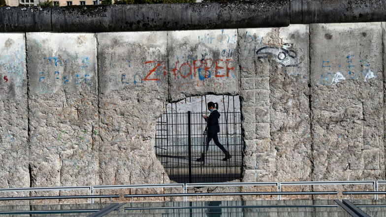 Steinerner Zeuge der Teilung: Eine Frau ist durch ein Loch der ehemaligen Grenzmauer in Berlin zu sehen.