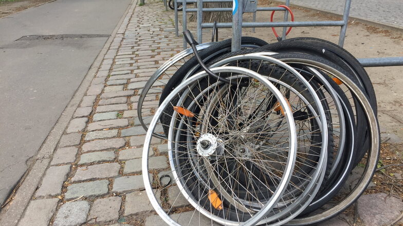 Zurückgelassene Vorderräder stehen an einer Straße und sind angekettet. Gegen Fahrraddiebstahl helfen vor allem sichere Abstellplätze. Foto: dpa/Marcus Brandt