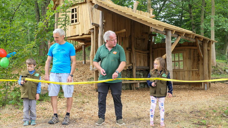 Der Erbauer Frank Große (links) und Peter Pachl, Geschäftsführer der Naturpark Zittauer Gebirge GmbH, eröffnen mit zwei Kindern das neue Baumhaus im Naturparkgarten in Waltersdorf.