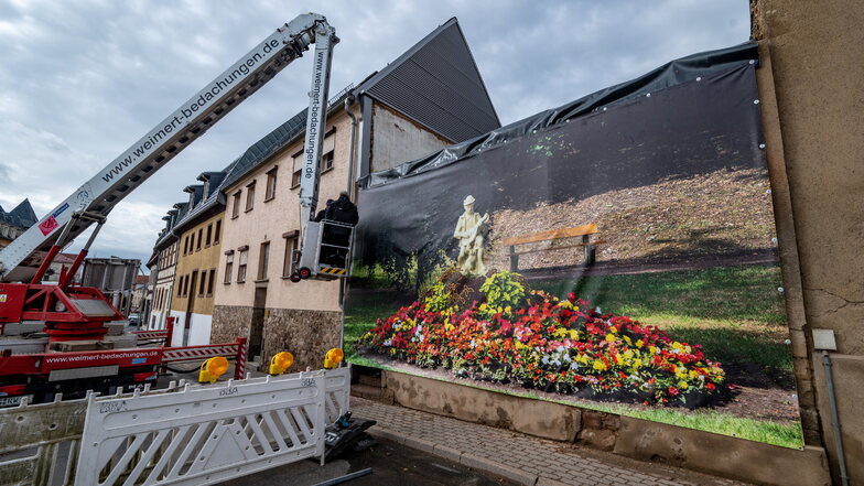 Mitarbeiter der Firma Weimert haben eine Plane vor eine der Hausruinen gehängt. Das Foto vom Lautenspieler im Bürgergarten stammt vom Fotografen Lutz Weidler.