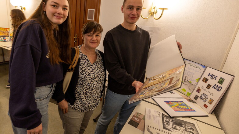 Schwester Arielle Erhardt und Mutter Silke lassen sich von Ephraim (v.l.) sein Kunstbuch aus dem Leistungskurs des Großenhainer Gymnasiums zeigen. Bilder der Schüler sind derzeit in einer Ratshausausstellung zu sehen.