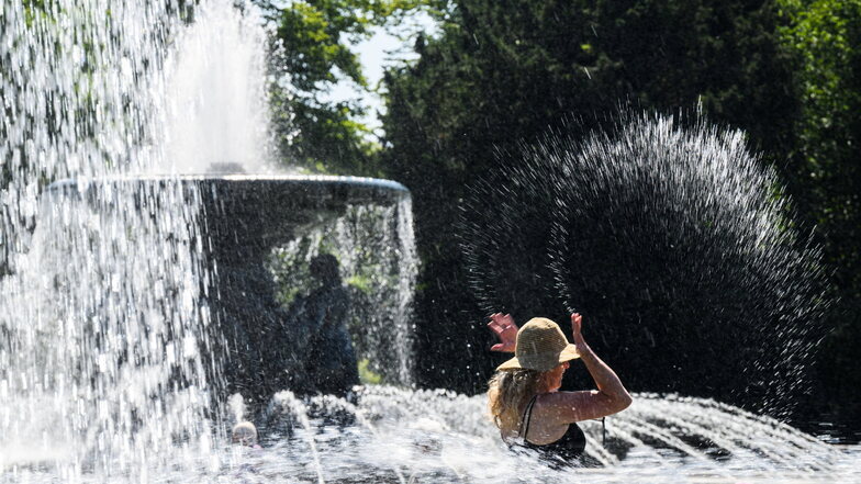 Eine Frau kühlt sich am Albertplatz an den Wasserfontänen ab. Das Betreten der Dresdner Brunnen ist verboten.