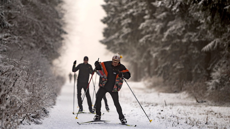 Wintersportler auf Langlaufskiern sind im verschneiten Naturpark Hoher Meißner in Hessen auf einer gespurten Loipe unterwegs.