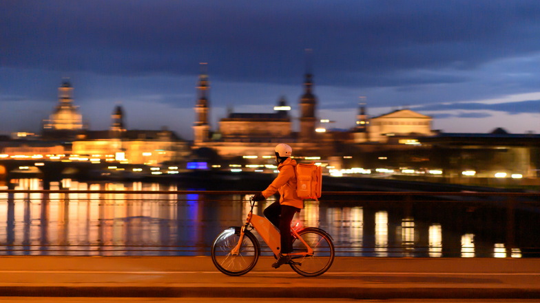 Ein Fahrrad Kurier des Lieferdienstes "Lieferando" fährt am Abend vor der Altstadtkulisse mit der Frauenkirche.