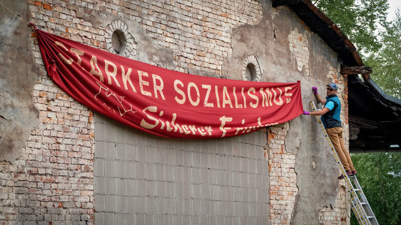 An einem Gebäude auf dem Roßweiner (Güter-)Bahnhofsgelände hängt ein Banner mit einer Parole aus DDR-Zeiten. Die wird für einen Filmdreh benötigt.