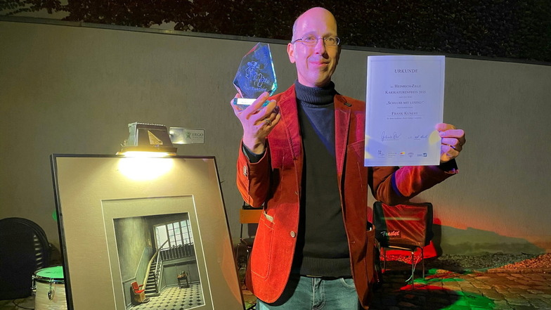 Frank Kunert mit dem Preis, der Urkunde und seiner Siegerarbeit „Hoch hinaus“ des Heinrich-Zille-Karikaturenpreises 2021 der Stadt Radeburg.