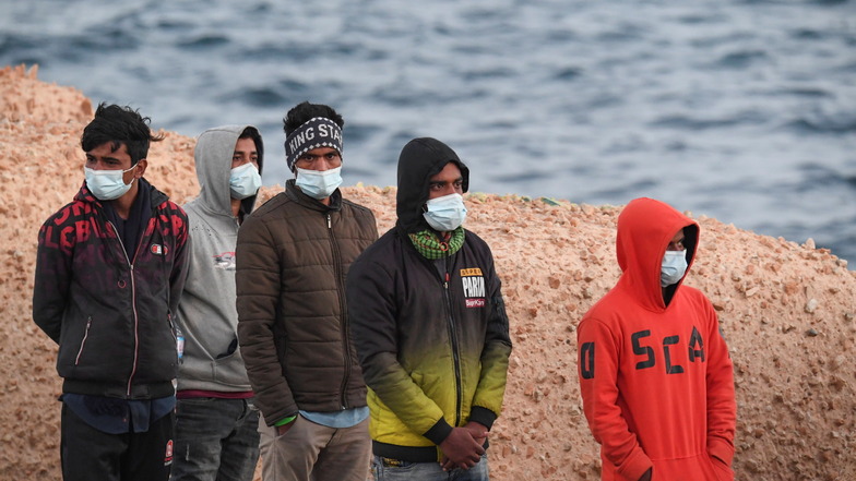 Migranten mit Mund-Nasen-Schutz stehen auf Lampedusa.