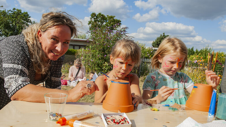 Anja Arlt-Lange vom Großenhainer Team der Outlaw gGmbH bemalte zur Garteneröffnung am Freitag mit Kindern Blumentöpfe – und Nele und Marlene (6) waren mit Feuereifer dabei.