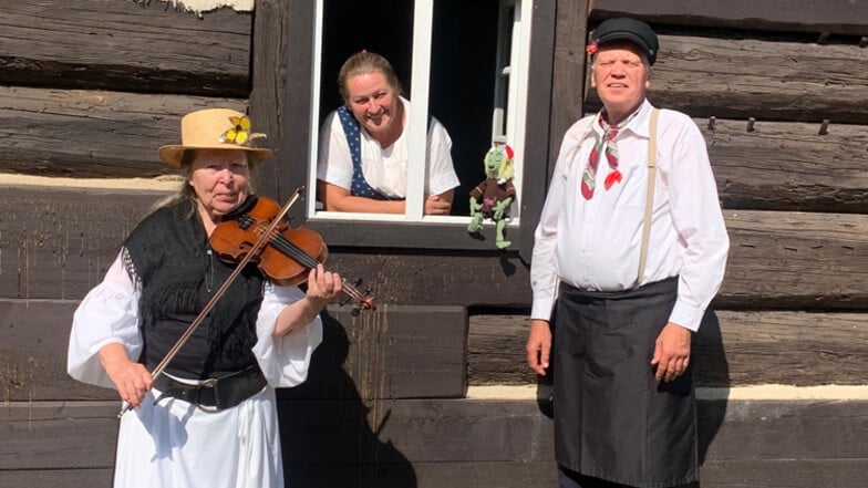 Gemeinsam in Lieske: Cornelia Schnippa schaut aus dem Fenster des Schrotholzhauses. Rechts ist Christoph Ruhland, links Inge Blümel mitsamt Geige.