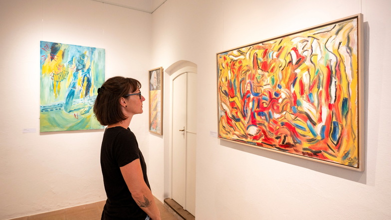 Eine junge Frau betrachtet in der Ausstellung "Seelenlandschaften" ein abstrakt-farbenfrohes Bild  von Manfred Queißer.