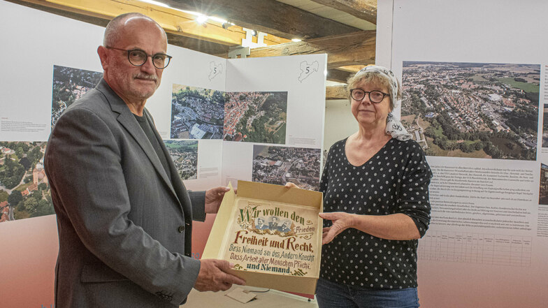 Der Kamenzer Oberbürgermeister Roland Dantz und Kuratorin Ragnit Michalicka zeigen ein Stickbild, wie es um 1920 typisch war. Es wird in der neuen Ausstellung im Malzhaus zu sehen sein.
