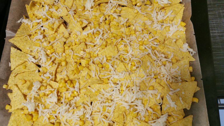 5. Schritt: Mais abtropfen lassen. Nachos auf einem Backblech (mit Backpapier bzw. Backunterlage) verteilen. Den Mais darüber und mit Käse bestreuen.