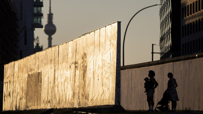 Eine Familie schaut sich an der East Side Gallery im Abendlicht ein Stück der Berliner Mauer an.