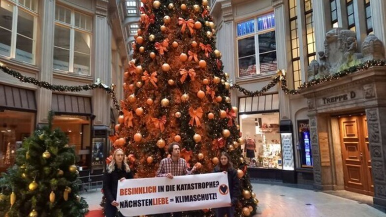 Prostestler der "Letzten Generation" stehen mit einem Banner vor dem besprühten Weihnachtsbaum in Leipzig.