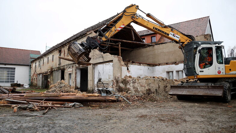 Ein Bagger sortiert mit seinem Greifer die Holzbalken aus dem alten Gebäude in Glaubitz, das momentan abgerissen wird.