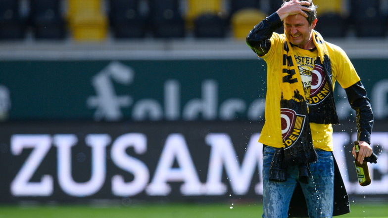 Eine Flasche Bier in der Hand und mindestens eine im Haar und auf dem Aufstiegs-T-Shirt: Dynamos Sportgeschäftsführer Ralf Becker feiert nach dem Abpfiff mit der Mannschaft im Stadion, erst später erfährt er, was davor wirklich los war.