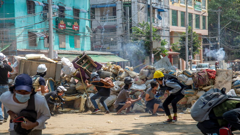 Demonstranten in Yangon, die gegen den Militärputsch demonstrieren, ducken sich, Schutz suchend, hinter einer Straßenbarrikaden, während die Polizei Geschosse abfeuert.