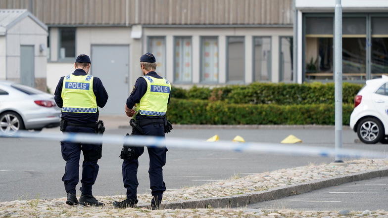 Zwei Polizisten stehen am Tatort nach mutmaßlichen Schüssen in Kristianstad auf einem Parkplatz.