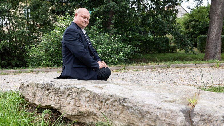 Ortsvorsteher Jörg Paulusch sitzt auf einem Stein, der laut Denkmalpflegern aus der Napoleon-Zeit stammt und als Brücke über einen kleinen Bach diente. Er soll künftig wieder als Brücke dienen.