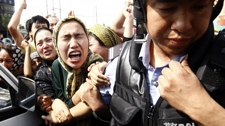 Eine Angehörige der uigurischen Minderheit in China versucht einen Polizisten zu packen, während einer Demonstration in Ürümqi in der Unruheregion Xinjiang in Nordwestchina im Jahr 2009.