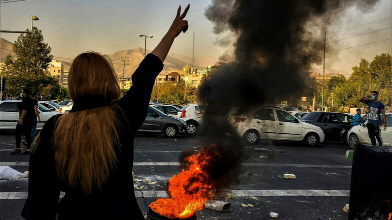 Eine Frau steht während einer Demonstration nach dem Tod der 22-jährigen Mahsa Amini vor einem brennenden Autoreifen in Teheran und zeigt das Victory-Zeichen.