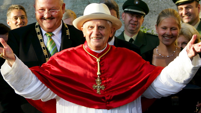 11.09.2006 Damaliger Papst Benedikt XVI. breitet an der Altöttinger Basilika mit einem Sonnenhut auf dem Kopf die Arme aus; Hut hat das Kirchenoberhaupt zuvor von Altöttings Bürgermeister Herbert Hofauer (l) geschenkt bekommen.