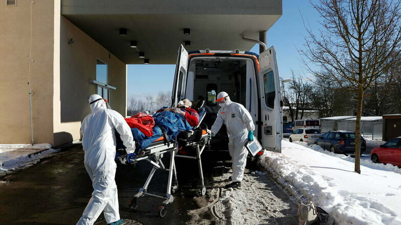 Medizinische Mitarbeiter in Schutzausrüstung transportieren eine Patientin auf einer Trage zu einem Krankenwagen vor einem Krankenhaus, das aufgrund einer hohen Anzahl an Coronapatienten überlastet ist.