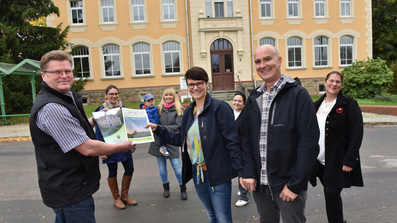 Der Dorfhainer Bürgermeister Olaf Schwalbe (li.) überreicht eine Willkommens-Mappe an Neu-Dorfhainer Sandra Appelt und Greg Ryan.