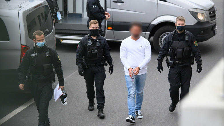 Einer der drei Tatverdächtigen wird von Polizisten in das Gebäude des Dresdner Oberlandesgerichts geführt.