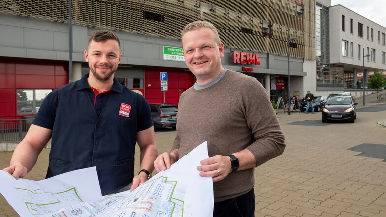 Marktleiter Tom Berger und Inhaber Björn Keyser (r.) halten den Bauplan in der Hand. Sie arbeiten derzeit an den Details für den Umbau des Rewe-Marktes neben dem Kultur-Bahnhof.