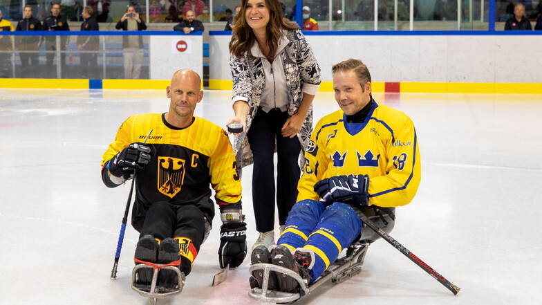 Umrahmt von Bas Disveld (l.), Kapitän der deutschen Nationalmannschaft und Peter Oiala, Kapitän der Schweden, darf Katarina, Witt den Eröffnungs-Bully für das Para-Eishockey-Länderspiel in Dresden machen.