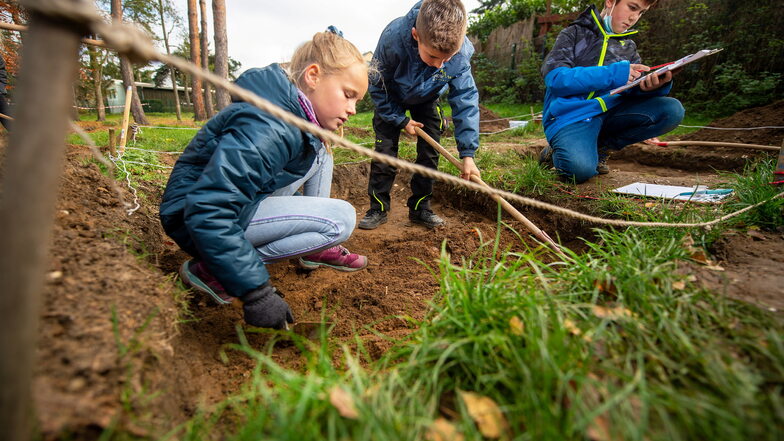 Charlotte, Moritz und Malte (v.l.) aus der Klasse 4a der Grundschule Graupa machen archäologische Ausgrabungen hinter dem Schulgebäude.