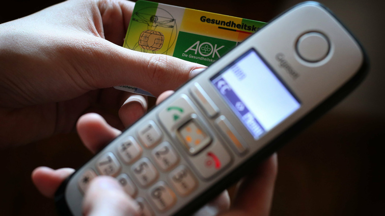 Ein Mann hält eine Gesundheitskarte der Allgemeinen Ortskrankenkasse (AOK) in der Hand, während er am Telefon eine Nummer wählt.