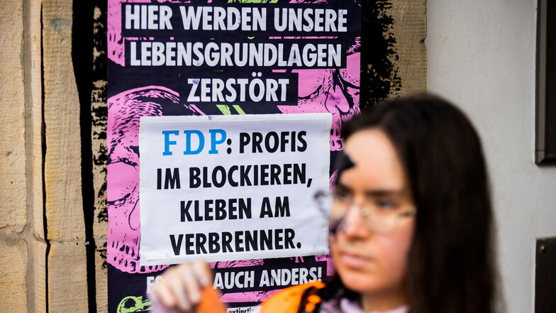 Ein Mitglied der Klimagruppe "Letze Generation" steht vor einem Plakat, nachdem die FDP-Bundesgeschäftsstelle mit ölartiger Farbe beschmiert wurde.