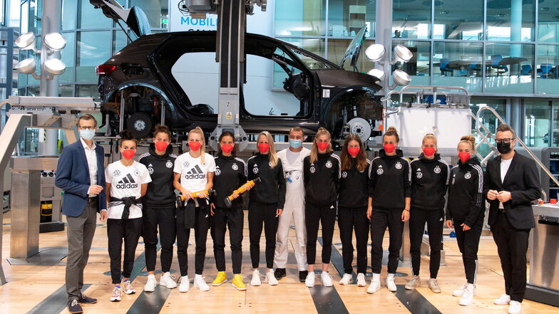 Die Spielerinnen der Frauenfußball-Nationalmannschaft stehen in der Gläsernen Manufaktur neben Danny Auerswald (l), dem VW-Standortleiter, vor einem Volkswagen ID.3.