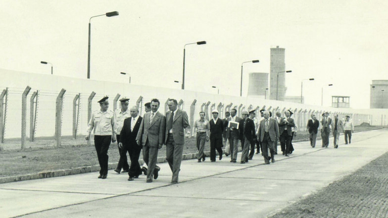 Die Strafvollzugseinrichtung Zeithain wird am 2. September 1977 eingeweiht. Der damalige Leiter führt dabei auch die Leitung der Abteilung Strafvollzug im Ministerium des Innern durch das Gefängnis. Im Hintergrund sind Türme des Rohrwerkes zu sehen.