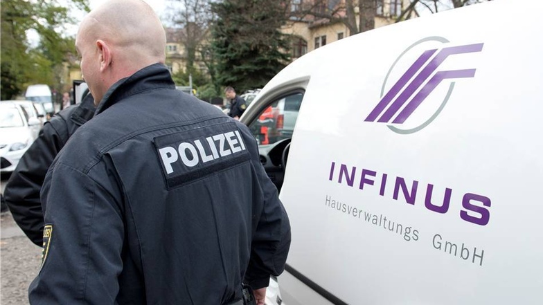 Ein Polizeibeamter steht während der Razzia in einem Objekt der Infinus AG am Vogesenweg in Dresden neben einem Fahrzeug der Firma.