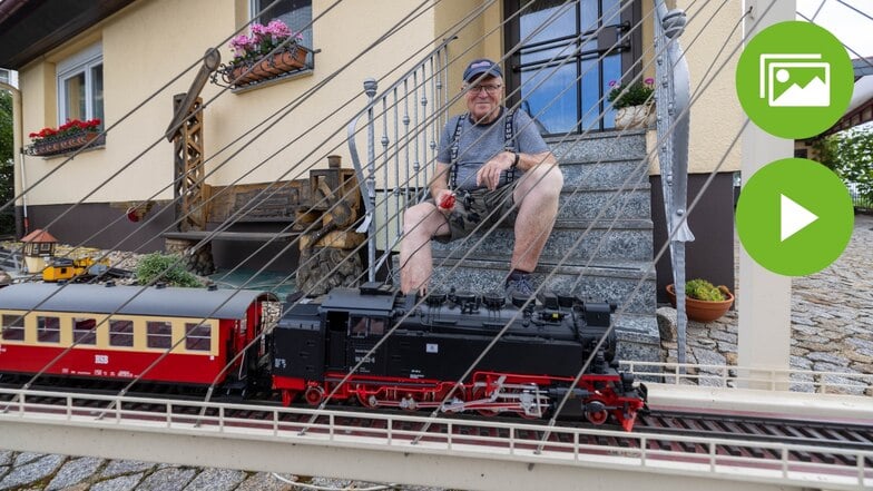Volker Hausmann sitzt auf der Treppe seines Hauses in Walda. Vor ihm fährt ein Zug seiner Gartenbahn über die Brücke.
