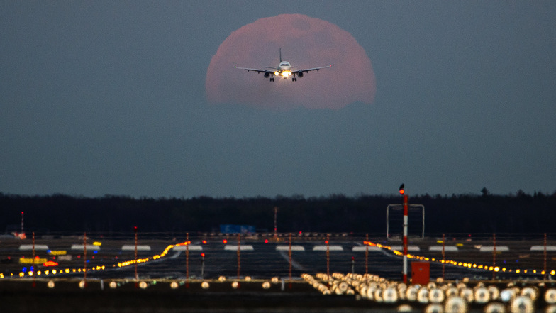 Ein Passagierflugzeug befindet sich am Frankfurter Flughafen im Landeanflug, während im Hintergrund der Vollmond aufgeht.