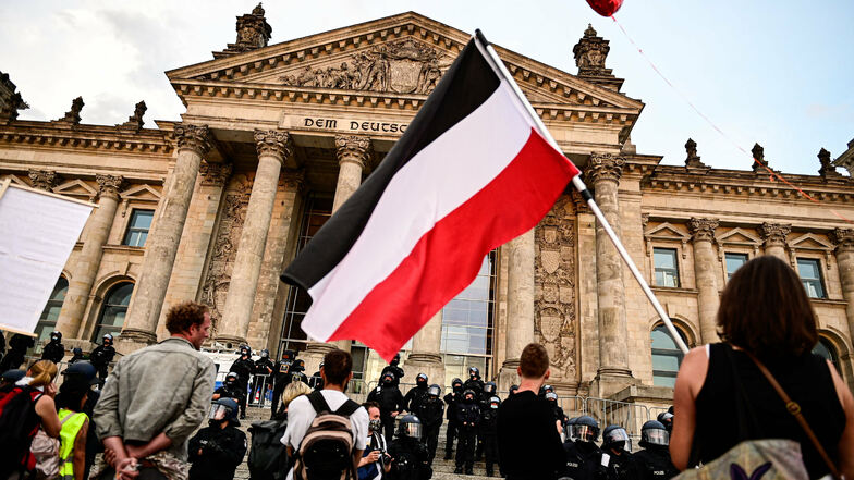 Teilnehmer einer Kundgebung gegen die Corona-Maßnahmen stehen vor dem Reichstag. Ein Teilnehmer hält die Flagge des 1918 untergegangenen Kaiserreiches.