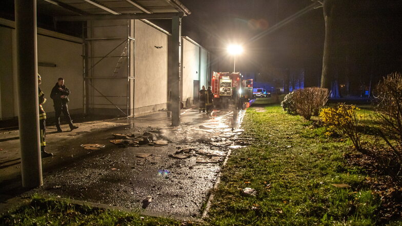 Einsatz in der Sonnabendnacht am Edeka-Einkaufskomplex in Niesky. Feuerwehrleute löschen einen brennenden Stapel Pappe.