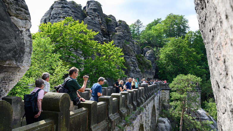 Touristen laufen im Nationalpark Sächsische Schweiz über die Basteibrücke. Im Hintergrund ist der Lilienstein zu sehen.