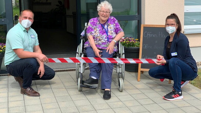 Die Tür wird symbolisch wieder freigegeben: Azurit-Bewohnerin Margit Hartmann freut sich auf die Lockerungen der Besuchsregelungen. Links ist Hausleiter Stefan Lux zu sehen, rechts Betreuungsleiterin Susann Doberentz.
